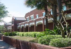 City Hall Red Brick building with columns, palm trees green bushes and a sidewalk