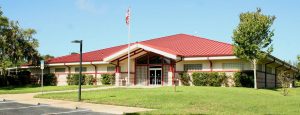 Police Department main building, red roof, yellow and brick building with green grass, trees, shrubs and a parking lot